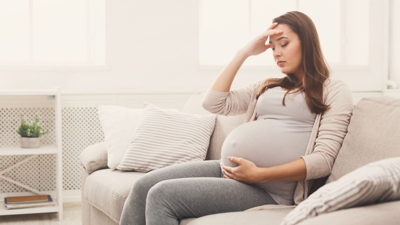 Thai phụ ngồi trên ghế sofa, tay đặt lên trán vì mệt mỏi, chóng mặt