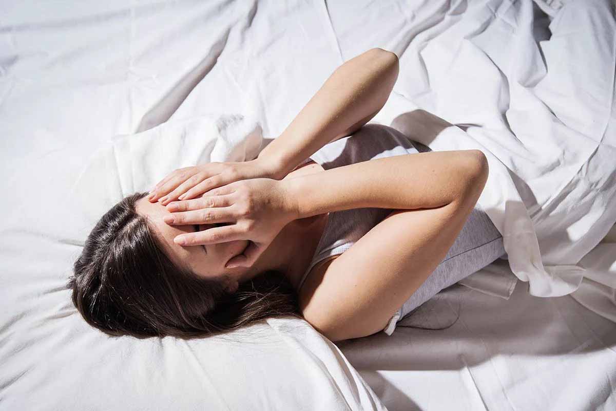 Người phụ nữ nằm trên giường lấy tay che mặt vì mất ngủ