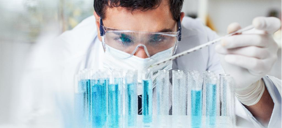 Kỹ thuật viên đeo kính bảo hộ dùng pipet thao tác trên giá ống nghiệm